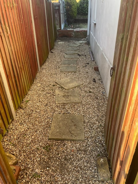Narrow outdoor alleyway between corrugated metal fences with stepping stones on gravel ground